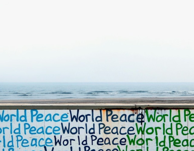 A seaside wall painted with the words “World Peace” repeated