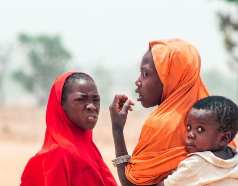 Two women in bright headscarves talking, one carrying a young child