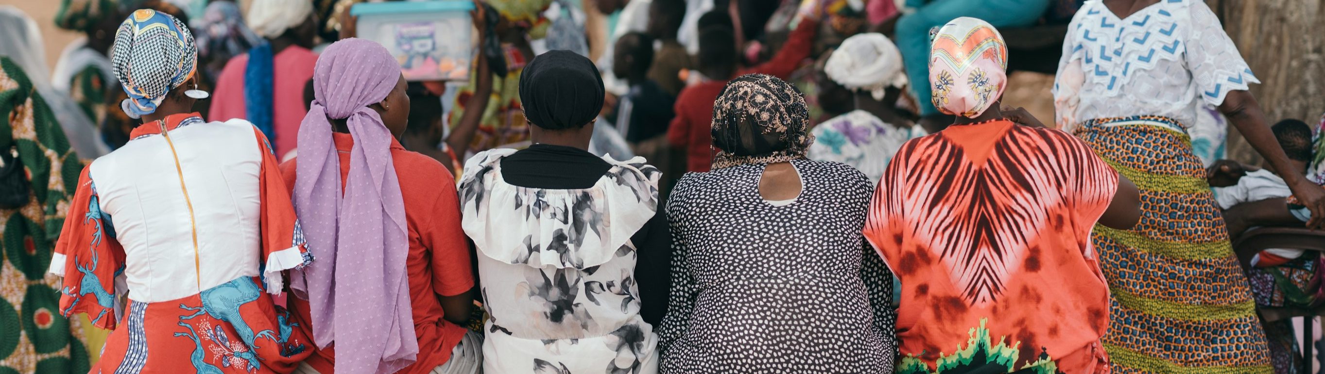 Women in colourful dress gathered at a community meeting, seen from behind