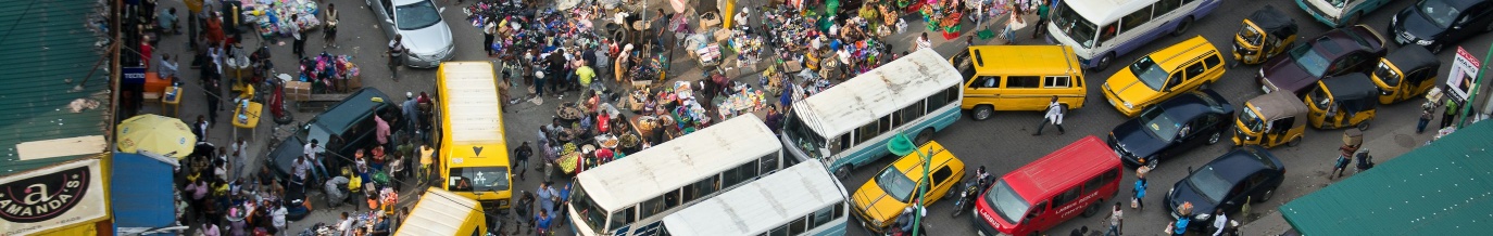 A busy West African market street crowded with buses, taxis and traders